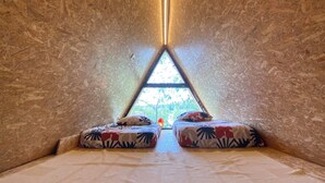 A cozy, triangular room with a slanted ceiling, a central light fixture, and a view of greenery outside.