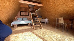 A loft bedroom with a wooden ladder, a bed, a desk, and a chair.