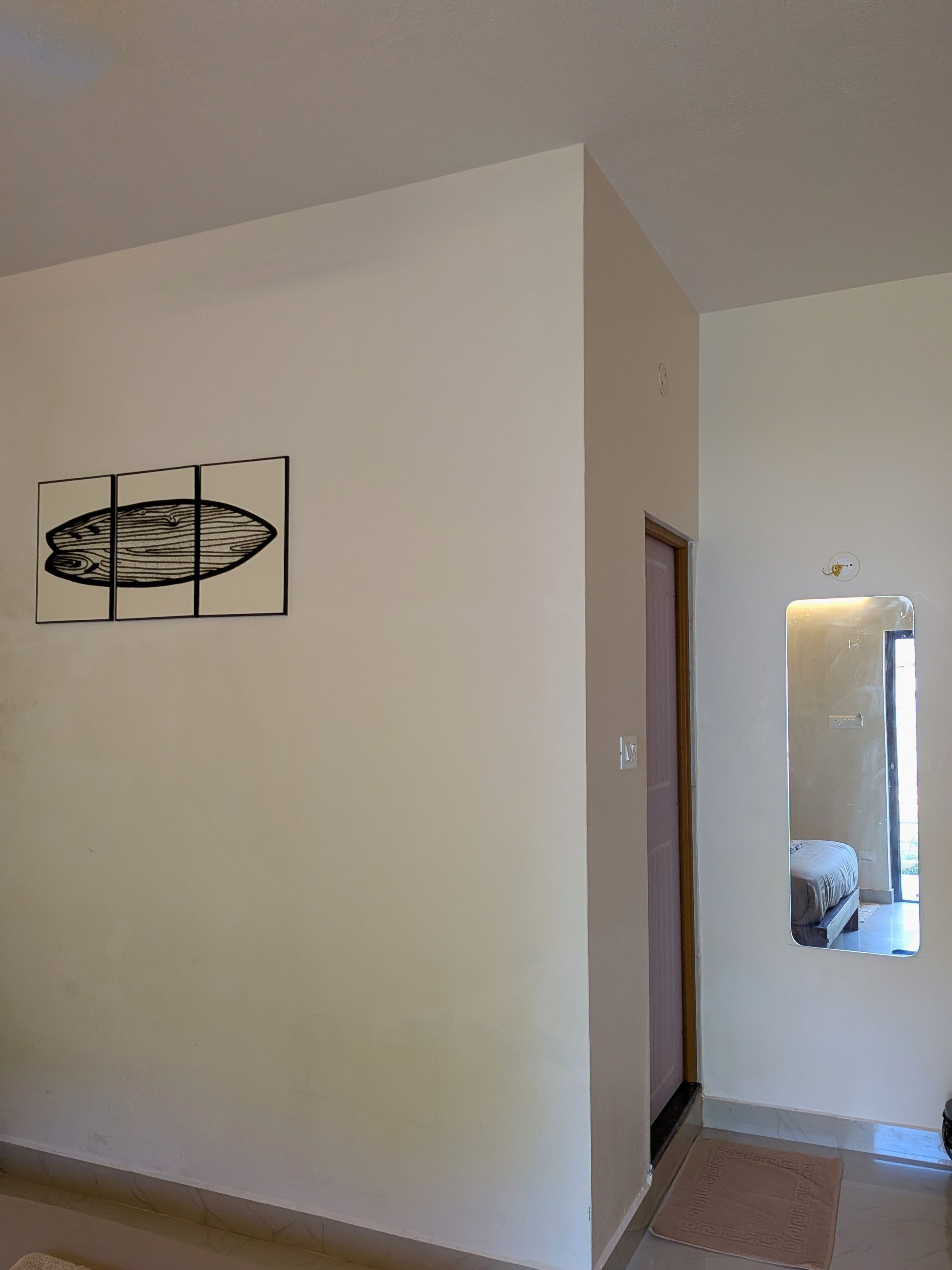A hallway with a door, a mirror reflecting a bed, and a wall-mounted artwork.