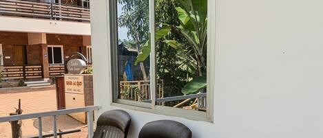 A balcony with two plastic chairs, a window with a view of greenery, and a sign indicating rooms are available.