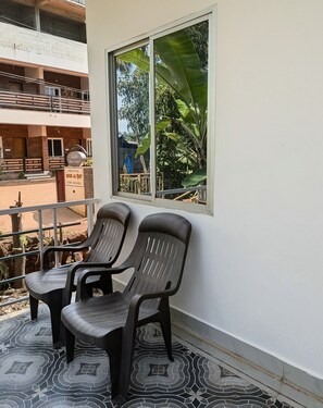 Un balcone con due sedie di plastica, una finestra che si affaccia sul verde e un cartello che indica camere disponibili.