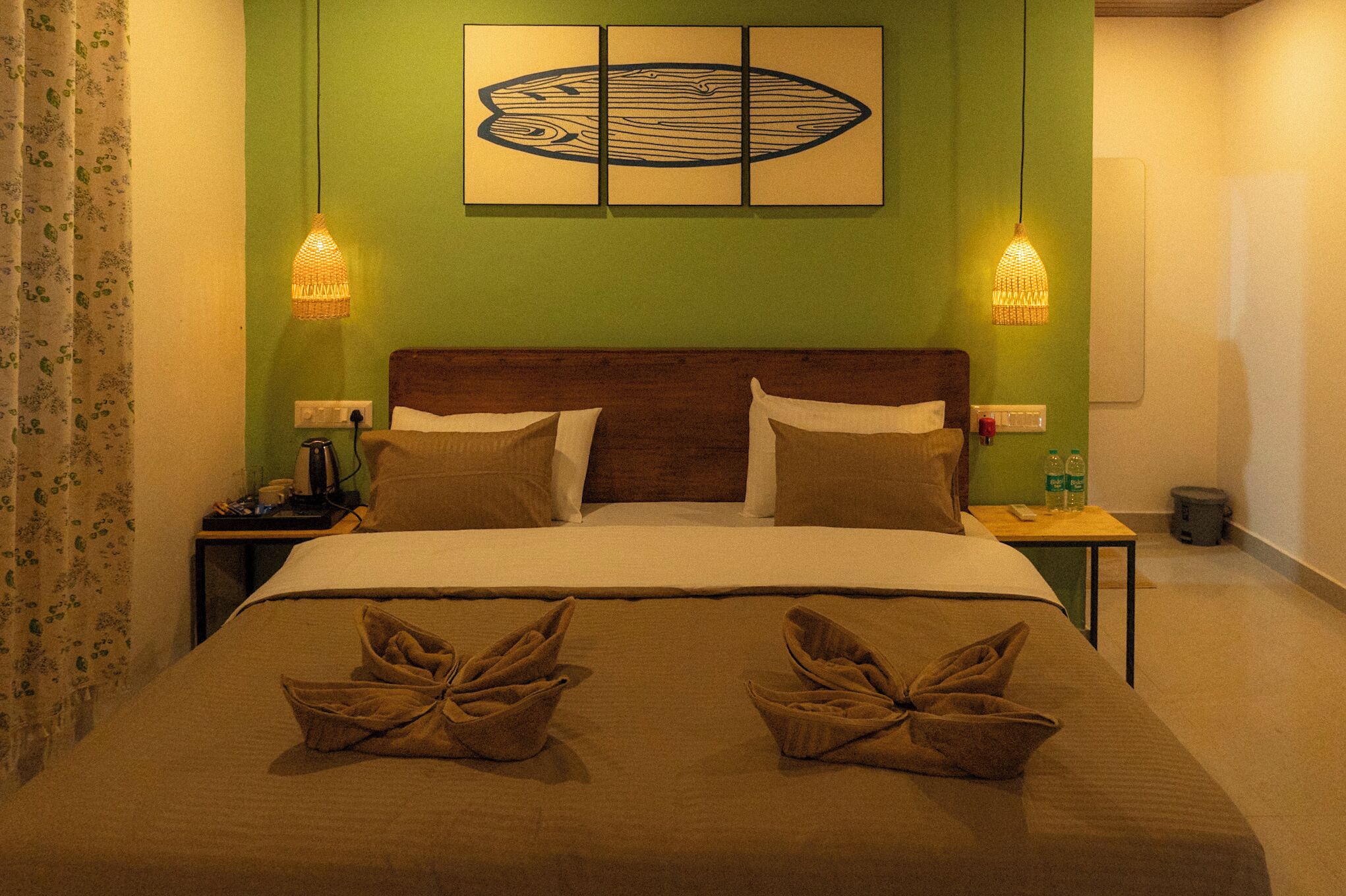 A hotel room with a green wall, a wooden headboard, a bed with two pillows, two bedside lamps, and a painting above the bed.