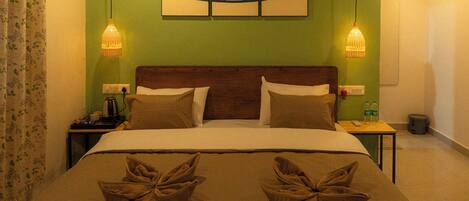 A hotel room with a green wall, a wooden headboard, a bed with two pillows, two bedside lamps, and a painting above the bed.