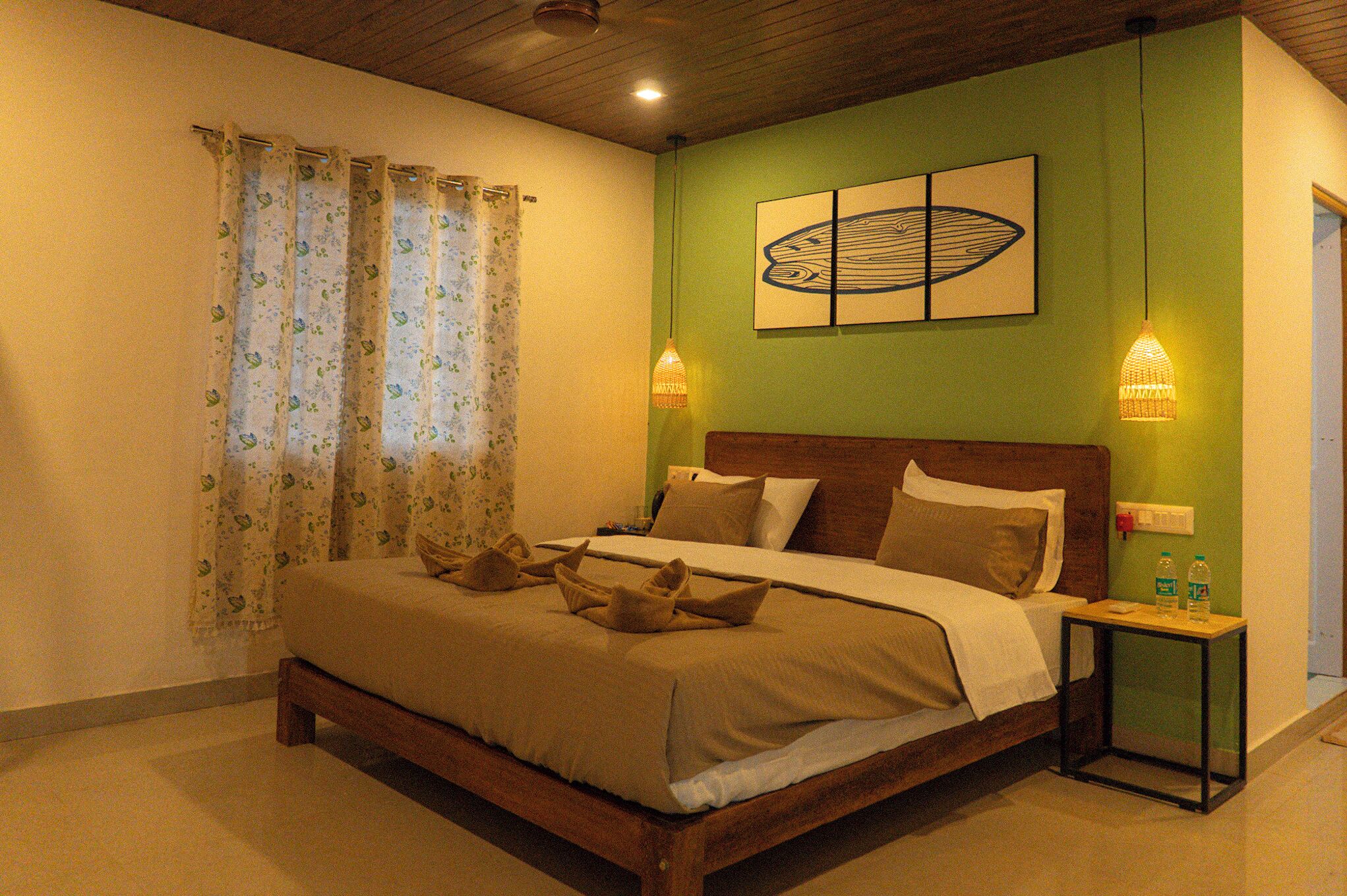 A neatly made bed with a wooden headboard, a green accent wall, and a framed artwork above it.