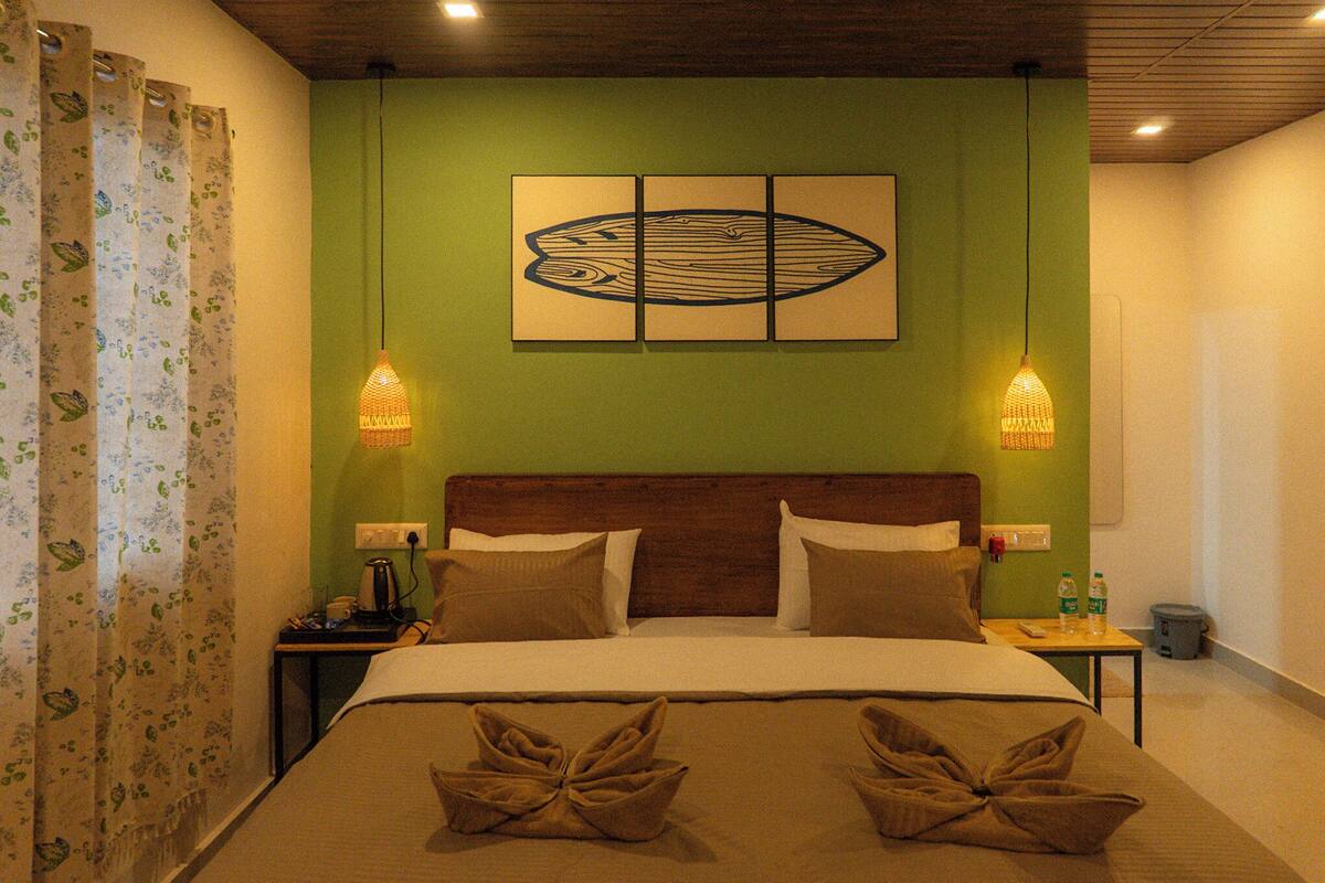A hotel room with a bed, green walls, a wooden headboard, two bedside tables, a wall art piece, and two hanging lamps.