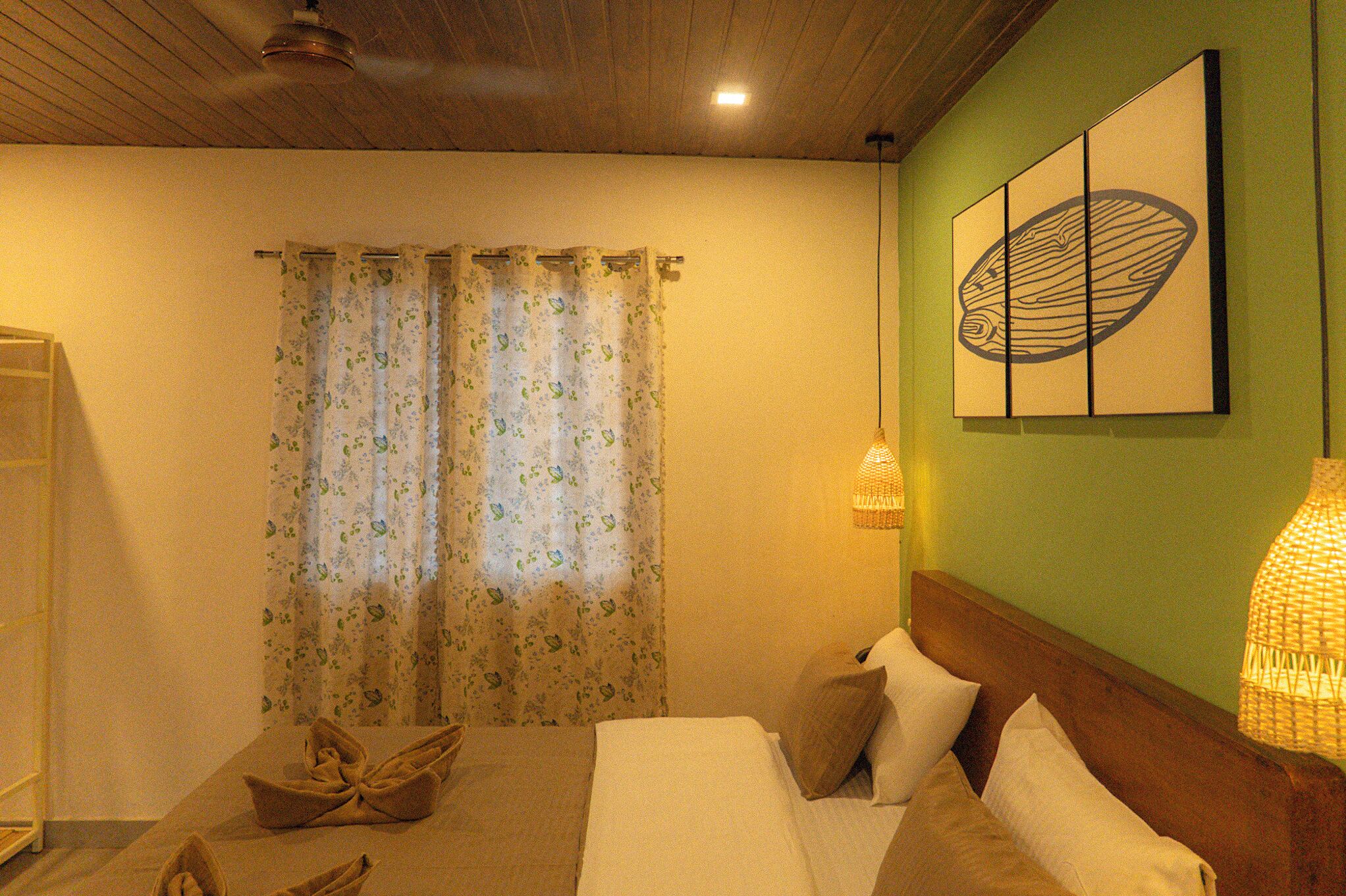 A bedroom with a bed, curtains, a wall-mounted lamp, and a painting.