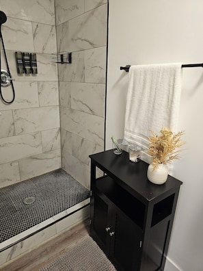 A bathroom with a shower, a black cabinet, a white vase with dried plants, and a towel hanging on a rack. - Chic, Clean, Comfortable Luxury for all (Cleveland)