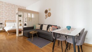 Een moderne woonkamer met een bank, een eettafel met stoelen, een boekenkast en een bed.