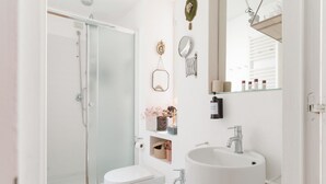 Een moderne badkamer met een douchecabine van glas, een wit wastafelmeubel en twee hygiënespotten.