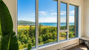 Ein Zimmer mit großen Fenstern und Blick auf eine Landschaft mit Bäumen und einem Gewässer.