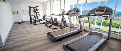 A gym with treadmills, stationary bikes, and weight machines, large windows with a view of the outdoors.