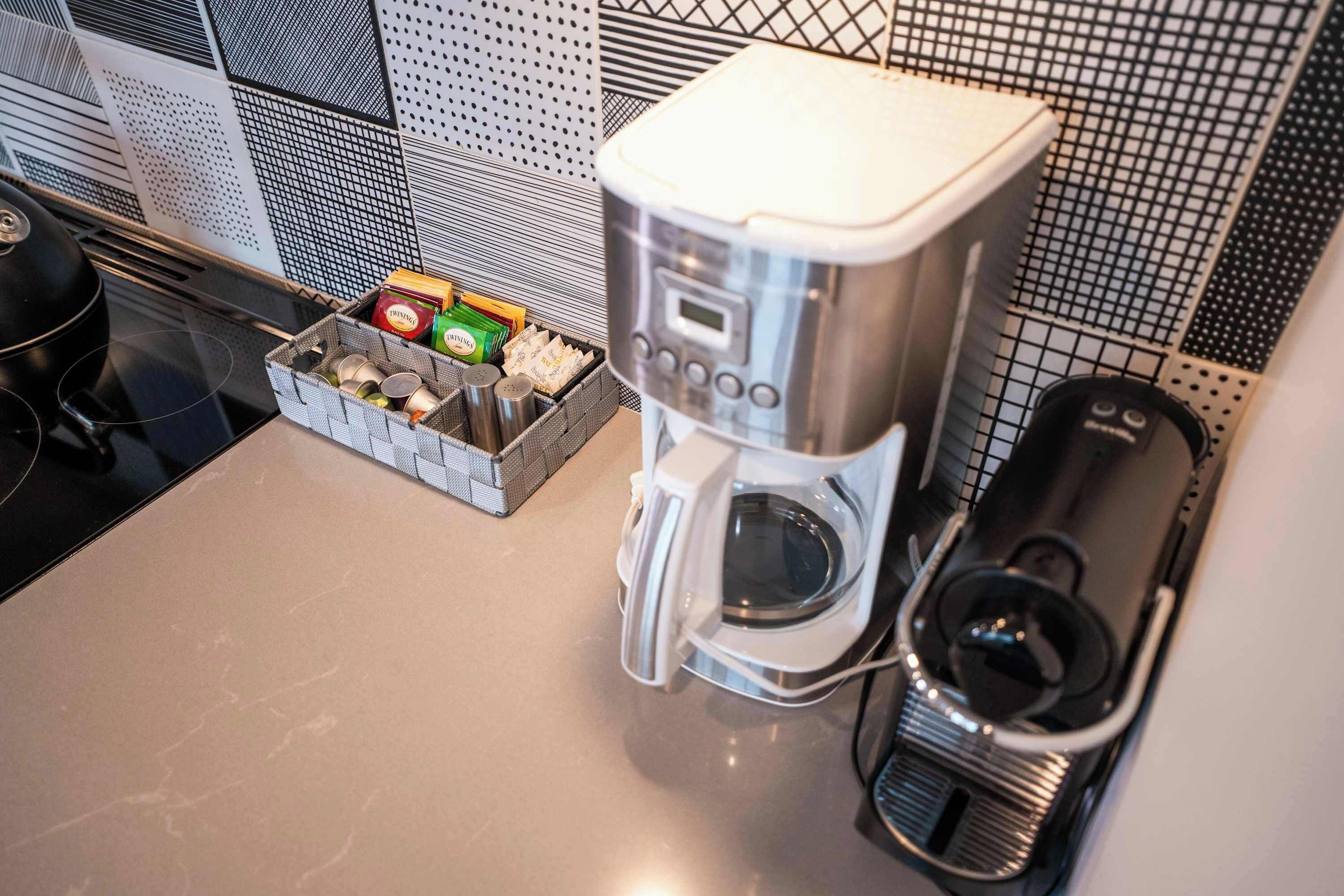 Een keuken met een koffiezetapparaat, een mandje met kruiden en specerijen, en een zwarte waterkoker.