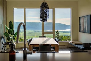 A dining area with a large table, chairs, a hanging light fixture, and a view of the outdoors. - 307 | Le Repere Condo | View and Modern Comfort (Baie-Saint-Paul)