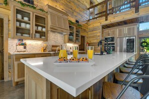 A modern kitchen with wooden cabinetry, a large island, and a breakfast setup with muffins and orange juice. - ATP~4Kings+bunkroom~Sleeps16~Pickleball~Hottub (Broken Bow)