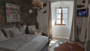 Un dormitorio con una cama grande, una pared de piedra, un reloj, un televisor y una alfombra de cuero de vaca.