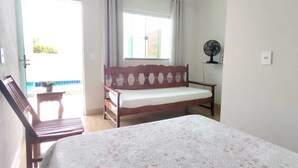 Een slaapkamer met een groot bed, een houten bankje, een klein tafeltje en een raam met gordijnen.