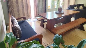 Een kamer met een houten eettafel, bankjes, een bank en een bloempot.