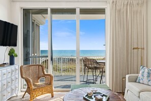 A balcony with a view of the ocean, wicker furniture, a white sofa, and a television on the left. - Spanish Key 107 (Pensacola)