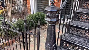Una escalera de metal negro con barandillas ornamentadas y un columnilla decorativa.