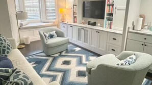Una sala de estar moderna con un sofá, dos sillones, una mesa de centro, un televisor y una estantería.
