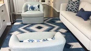 Un salón con un sillón azul claro, un sofá blanco y una alfombra estampada.