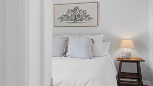 A bedroom with a bed, pillows, a bedside table with a lamp, and a framed picture on the wall.