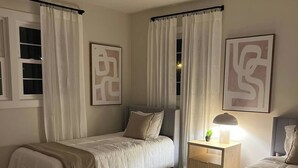 A bedroom with two single beds, a bedside table with a lamp, a rug, and artwork on the walls.