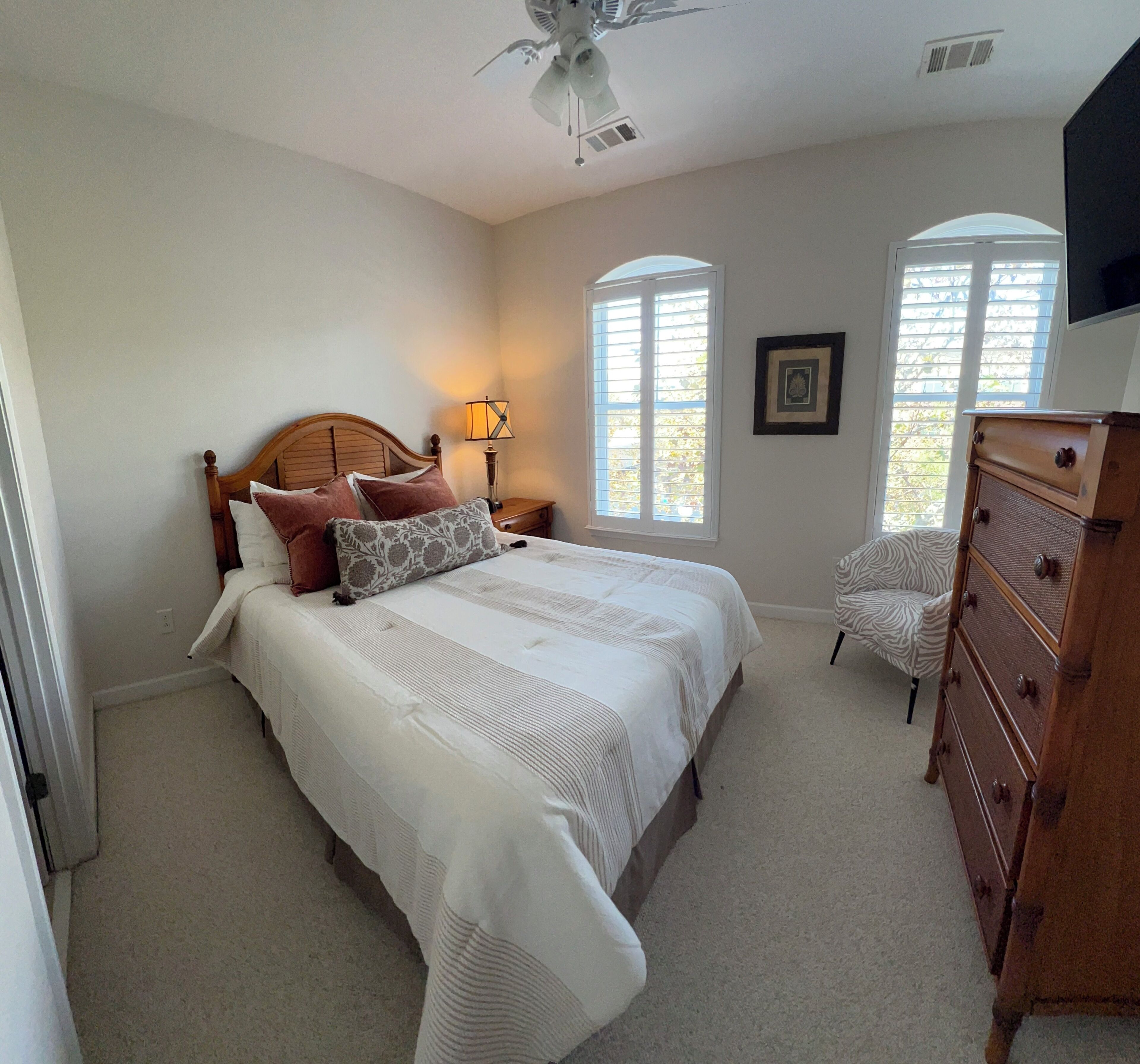 Ein Schlafzimmer mit Bett, Nachttisch, Kommode und Deckenventilator.