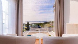 Varanda com mesa branca e duas cadeiras brancas, com vista para uma rua com carros e vegetação.