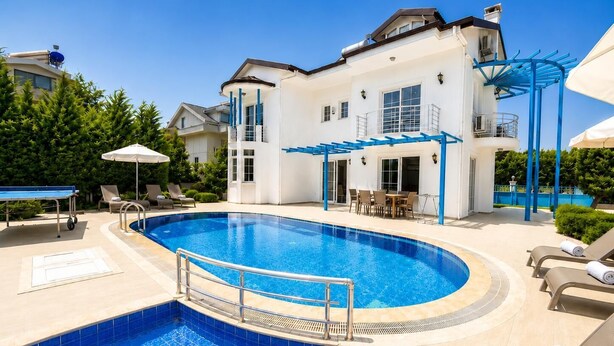 Ein Swimmingpool mit blau gefliestem Rand, Liegestühlen und einer überdachten Sitzgelegenheit im Freien.