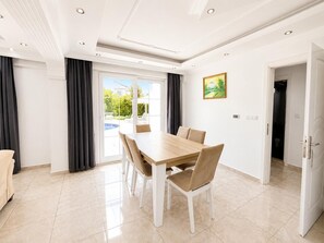 Un área de comedor con una mesa y sillas de madera, vista a una piscina y una puerta que da a otra habitación.