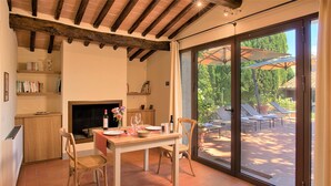 Un coin repas avec une table dressée pour deux personnes, une cheminée et une vue sur la terrasse extérieure.