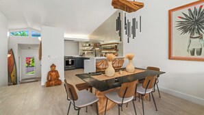 Et moderne spiseområde med et træbord og stole, en Buddha-statue og et køkken i baggrunden.