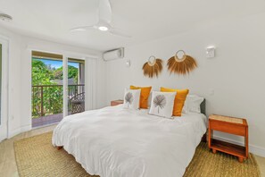 Ein Schlafzimmer mit einem großen Bett, einem Deckenventilator, einem Nachttisch und Blick auf einen Balkon mit Grünpflanzen.