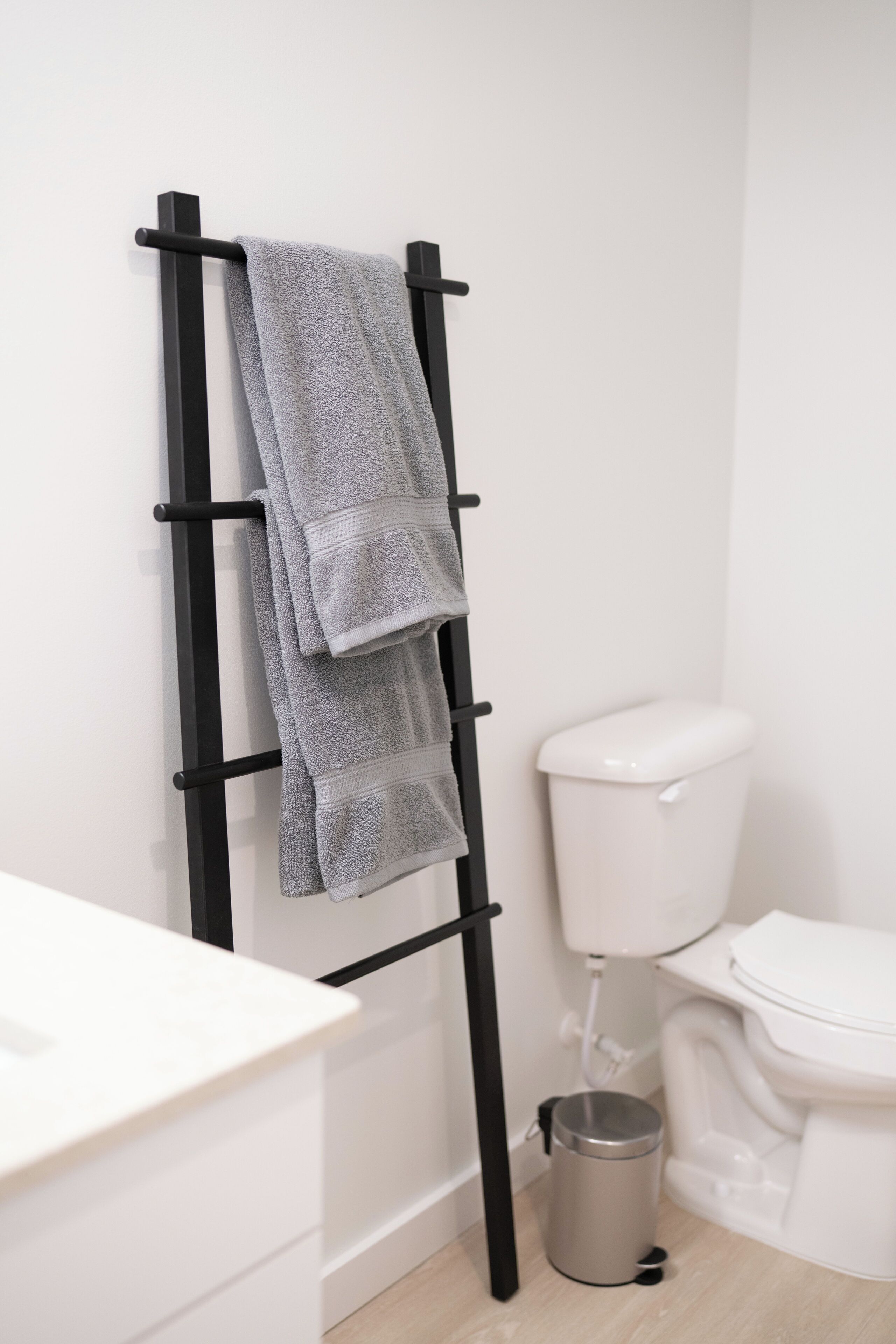 Un bagno con un porta asciugamani nero che contiene due asciugamani, un water bianco e un cestino.