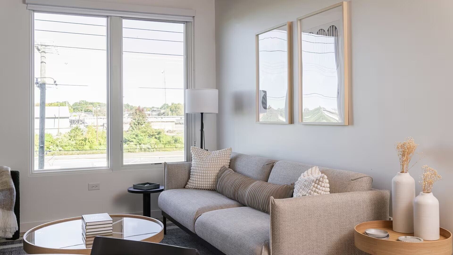 En moderne stue med sofa, rundt sofabord, lampe og indrammede billeder på væggen.