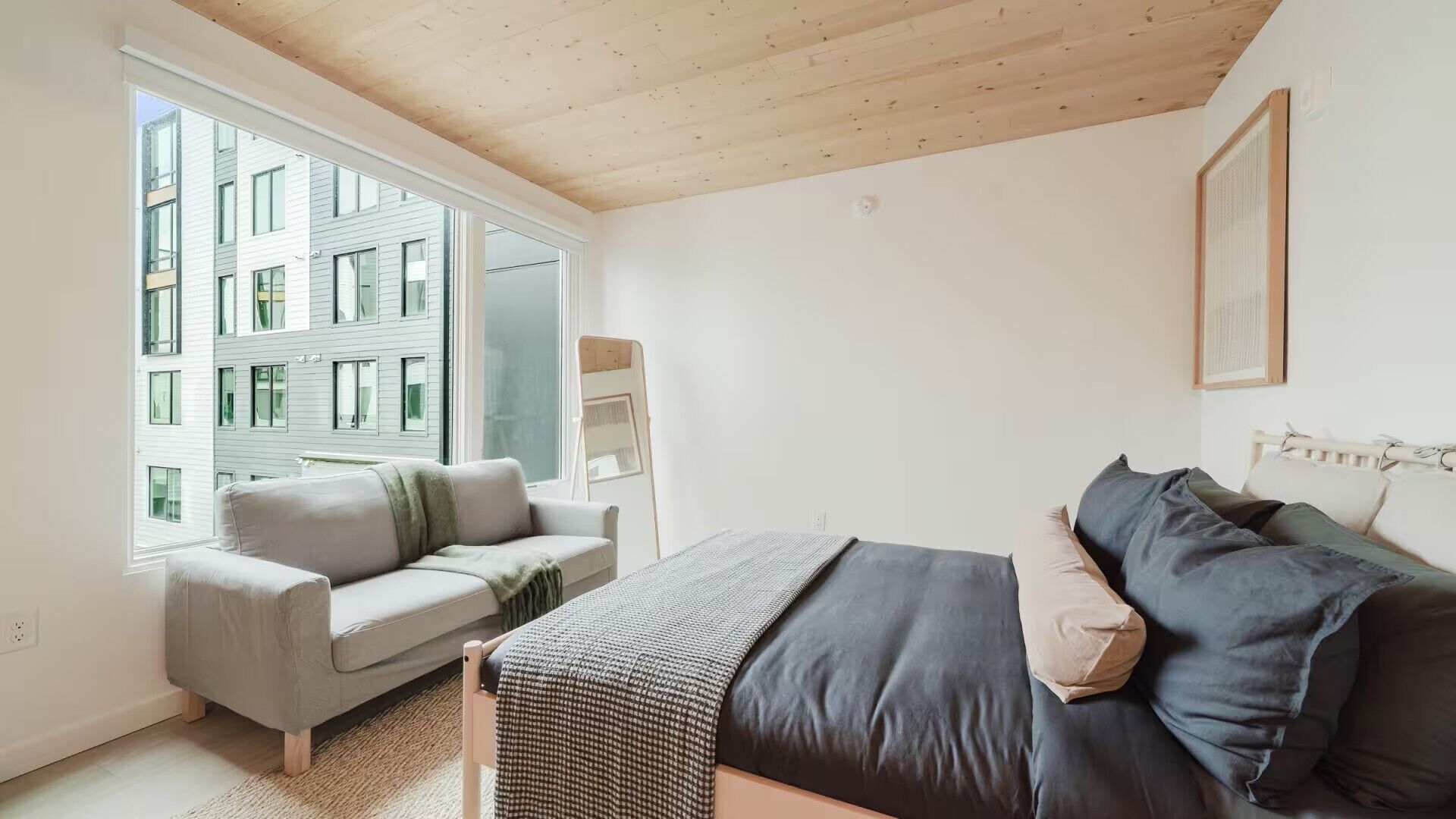 Ein modernes Schlafzimmer mit einer Couch, einem Bett, einem Fenster und Blick auf ein Gebäude.