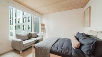 Ein modernes Schlafzimmer mit einer Couch, einem Bett, einem Fenster und Blick auf ein Gebäude.