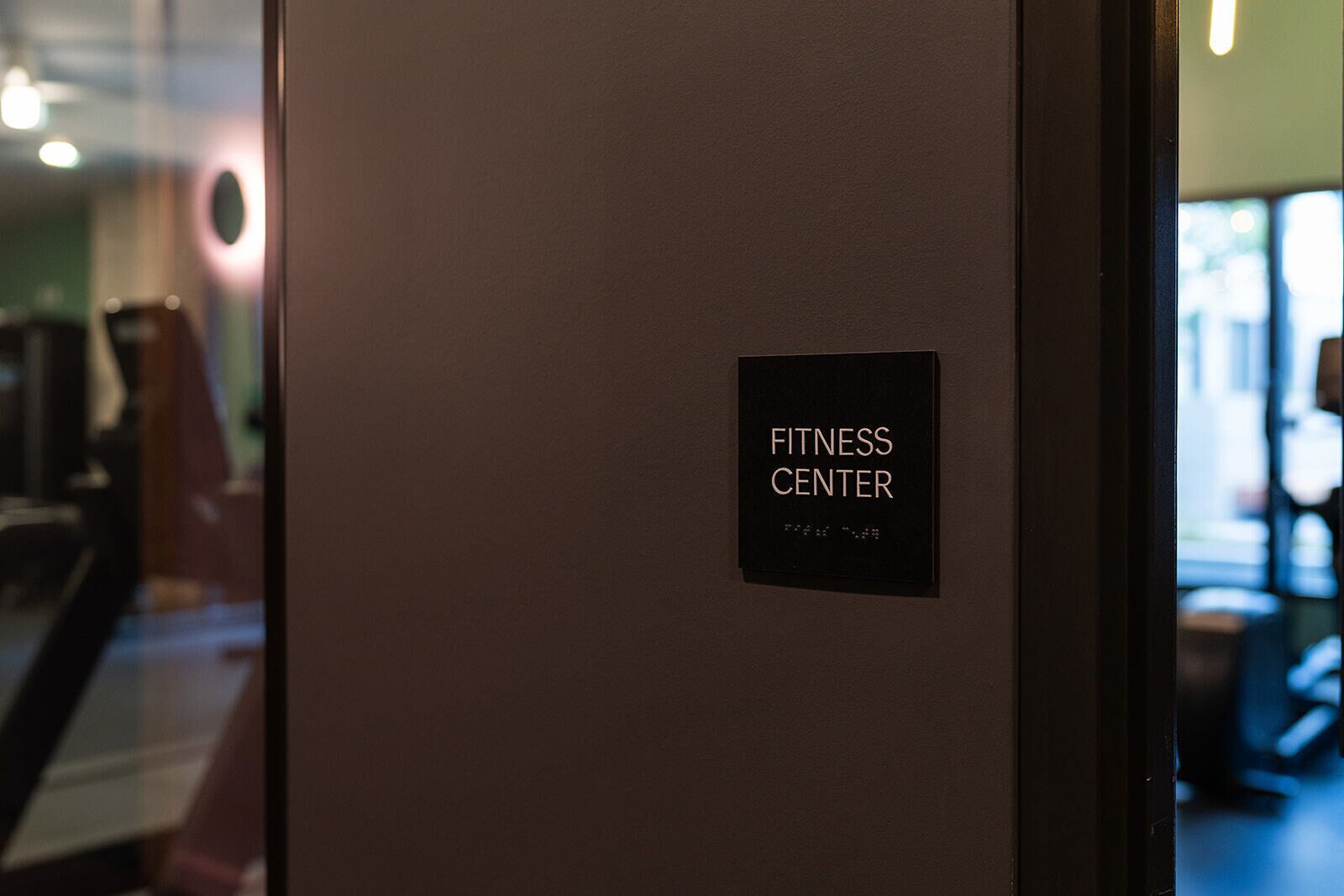 A door with a sign reading "FITNESS CENTER" and a partial view of a gym interior.