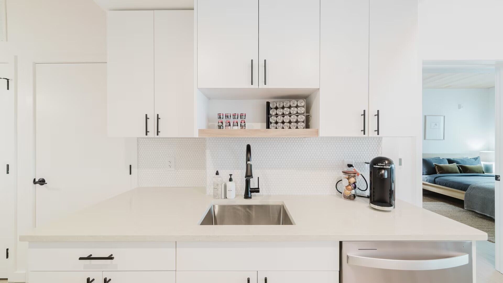 Une cuisine moderne avec des meubles blancs, un évier en acier inoxydable et une machine à café.