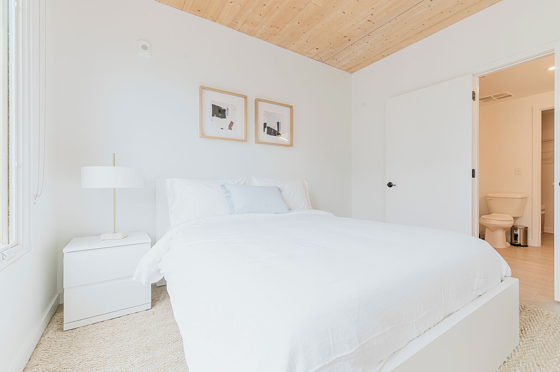 A bedroom with a bed, nightstand, lamp, and two framed pictures on the wall.