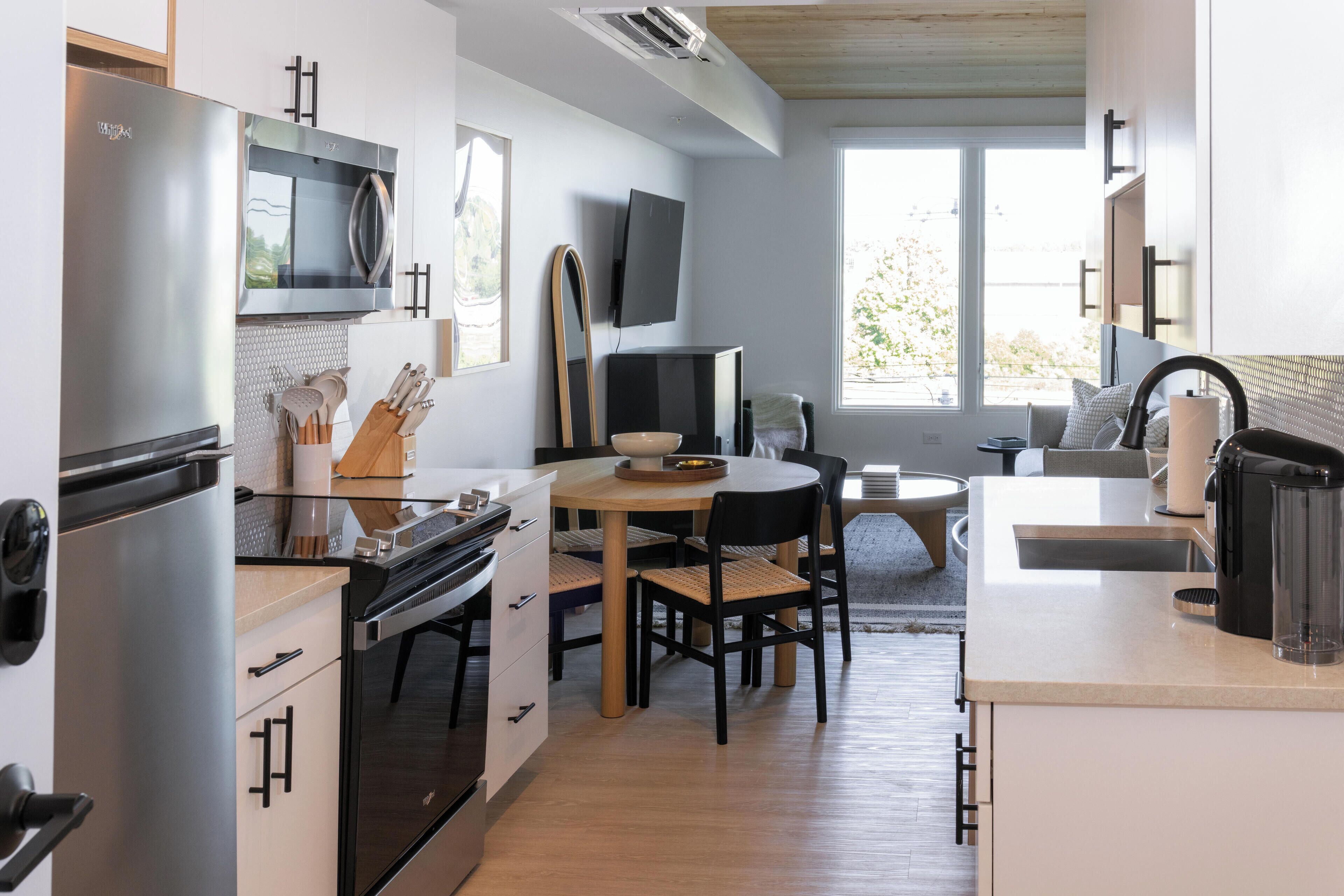 Eine moderne Küche mit Edelstahl-Kühlschrank, Mikrowelle und Backofen. Ein Esstisch mit Stühlen und ein an der Wand montierter Fernseher sind ebenfalls vorhanden.