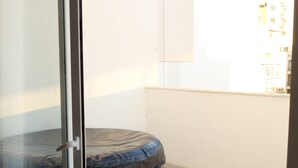 Et værelse med en skydedør, et overdækket udendørs siddeområde og udsigt til bygninger i baggrunden.
