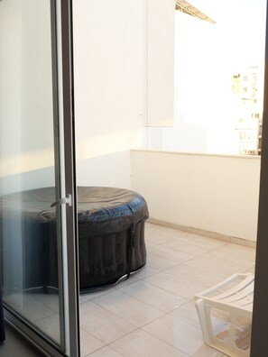 Ein Zimmer mit einer Schiebeglasdoor, einem überdachten Sitzbereich und Blick auf Gebäude im Hintergrund.