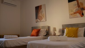 Et hotelværelse med to senge, hver med pude og dyne. Der er en lampe på natbordet og et billede på væggen.