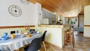 Een eetgedeelte met een tafel gedekt voor twee personen, een keuken op de achtergrond en een houten plafond.