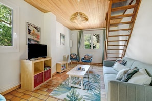 Uma sala de estar com televisão de tela plana, armários de madeira, uma mesa de centro, um sofá e uma escada.