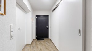 Ein Flur mit einer dunklen Tür, weißen Wänden und einem hellen Holzboden.