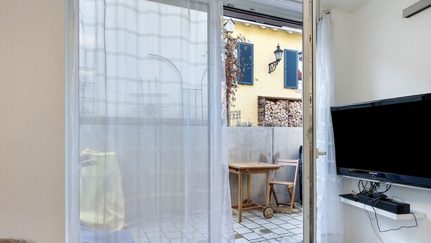 Ein Zimmer mit einer Schiebeglastür, einem an der Wand befestigten Fernseher und einem kleinen Tisch mit einem Stuhl.