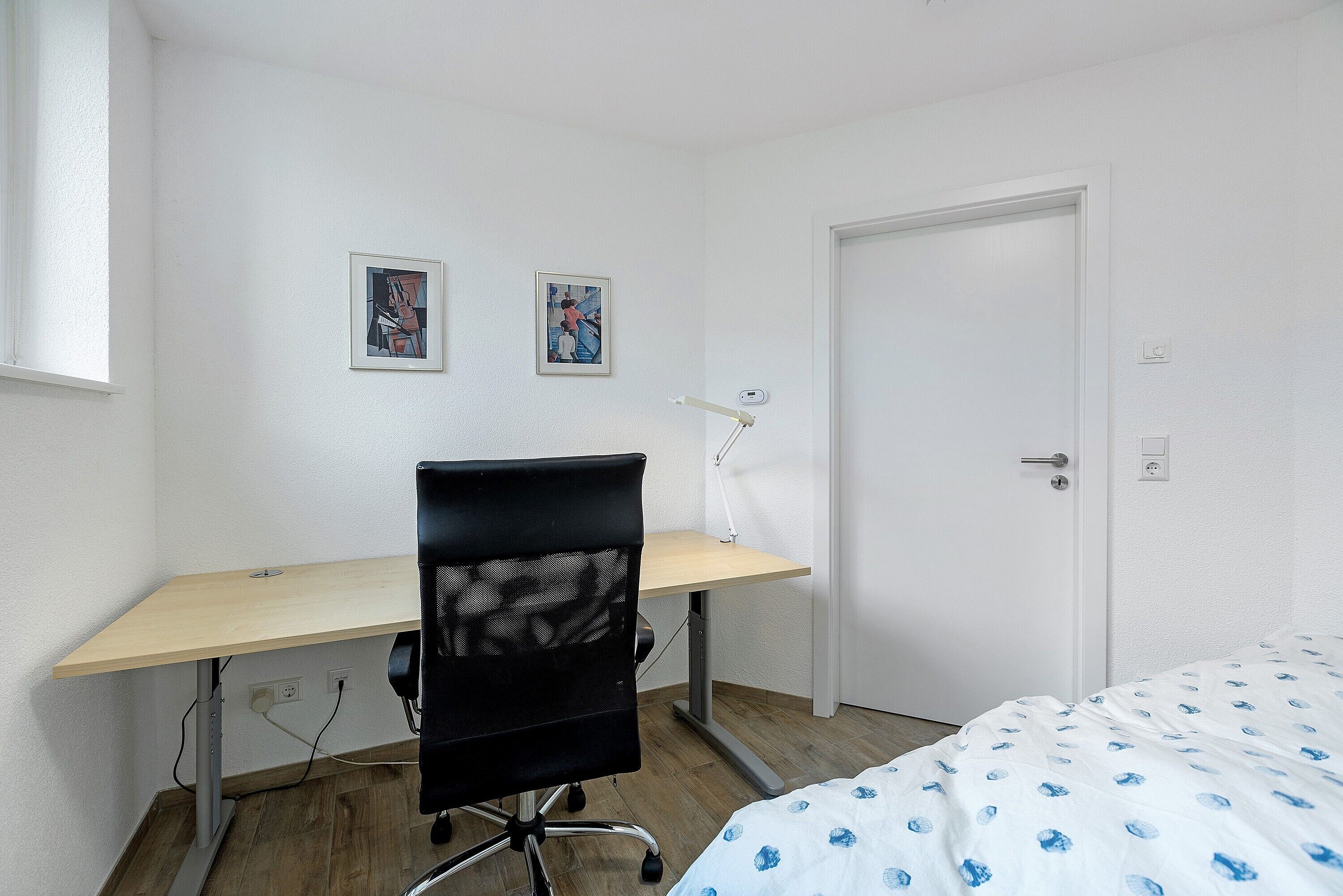 Een slaapkamer met een bed, een bureau en twee ingelijste foto's aan de muur.